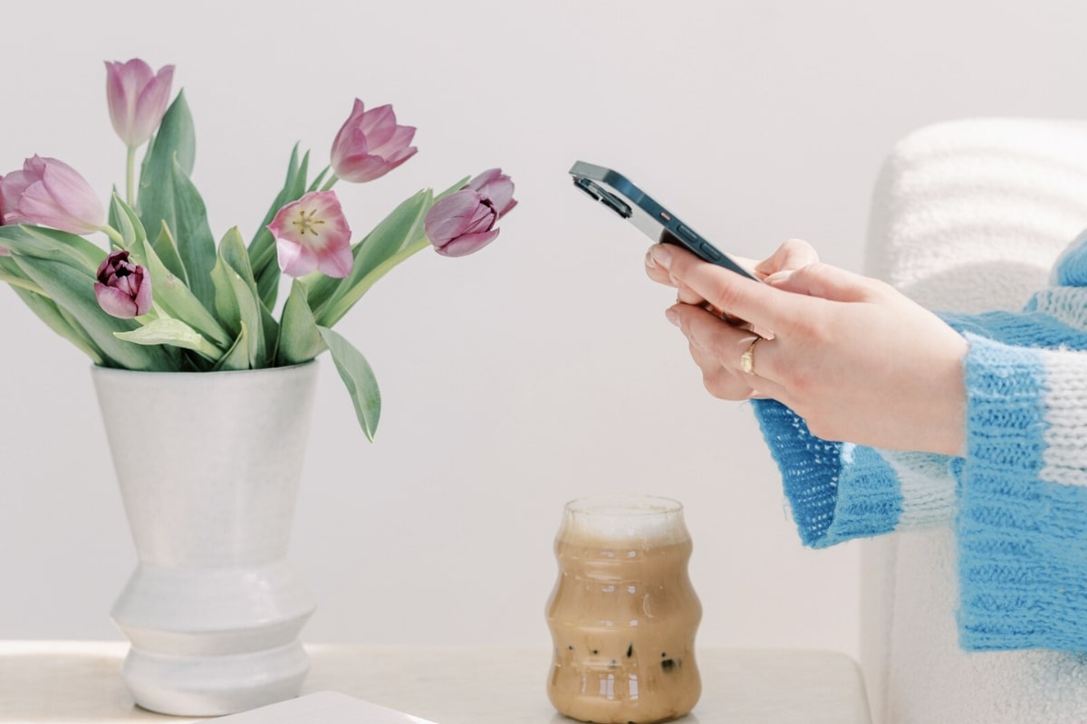 スマートフォンを両手で操作する女性の手元と花